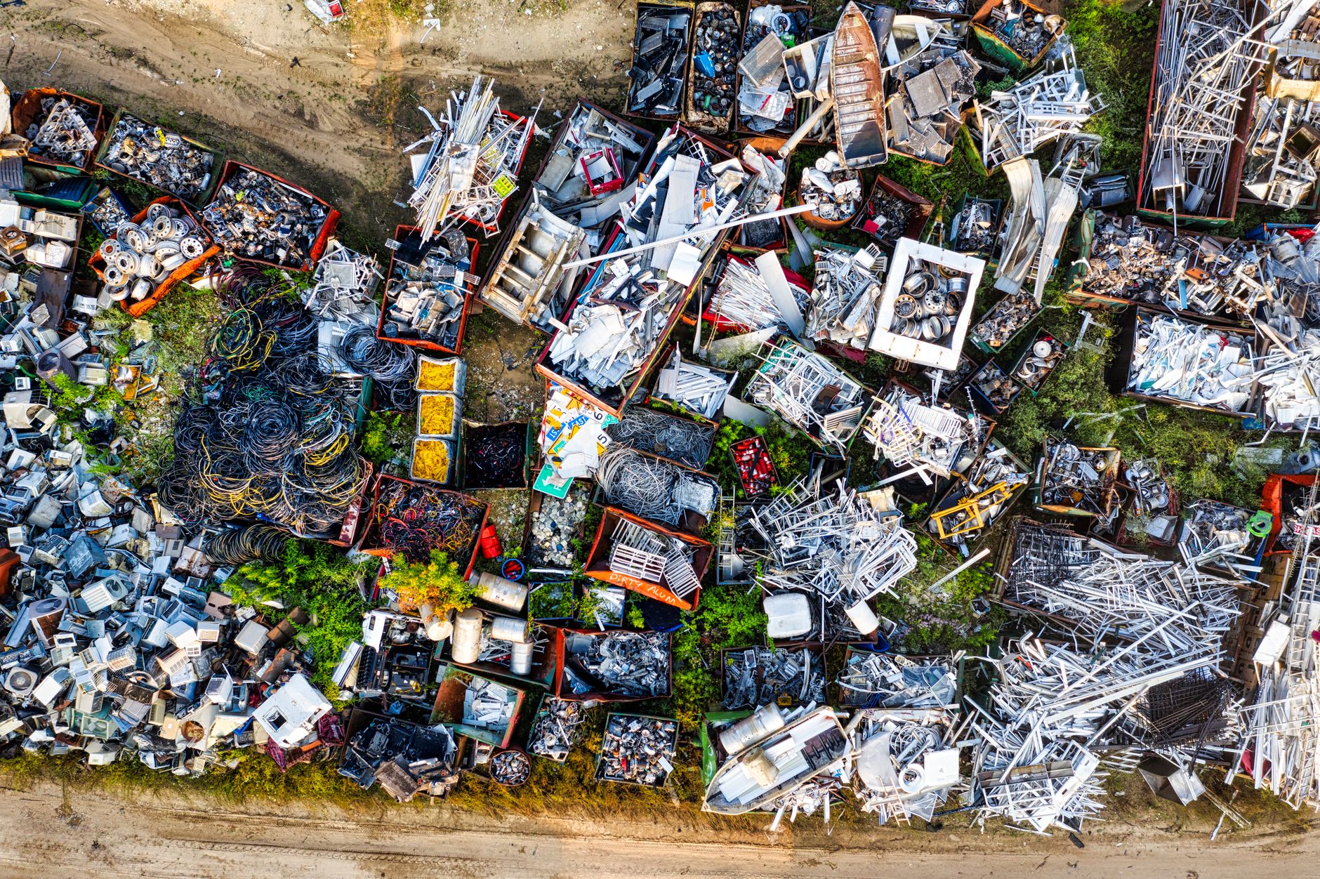 Sorted waste materials stacked at an outdoor recycling yard with tree lines in the background.