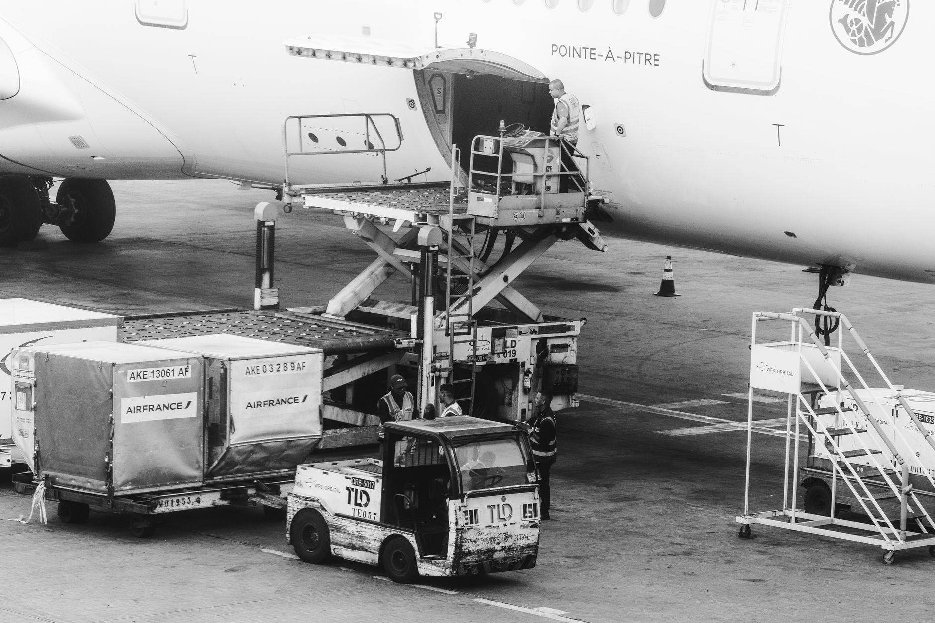 Freight handlers preparing air cargo shipments beside an airport warehouse.