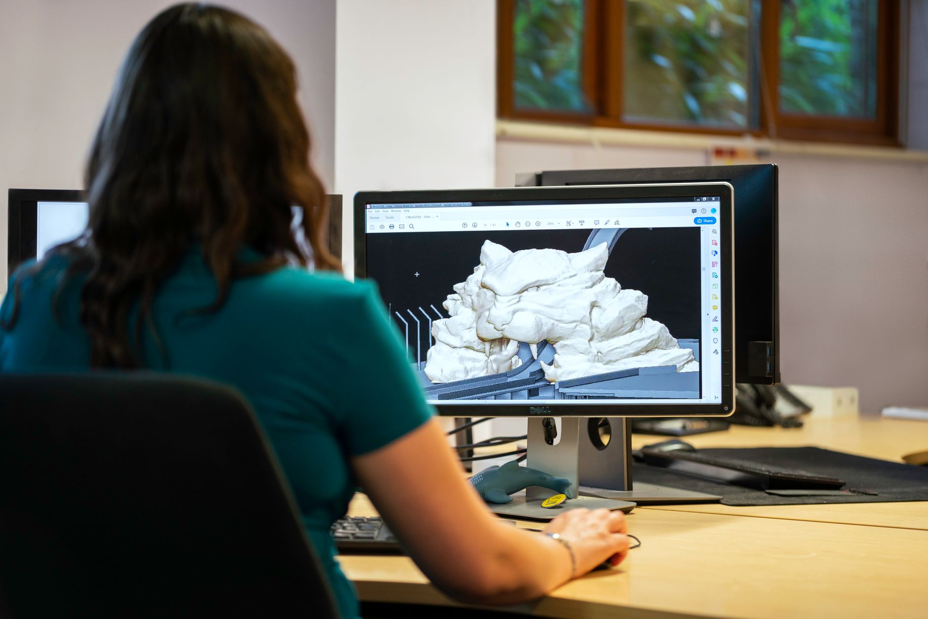 An engineer reviews component and factory-layout drawings at a CAD workstation.