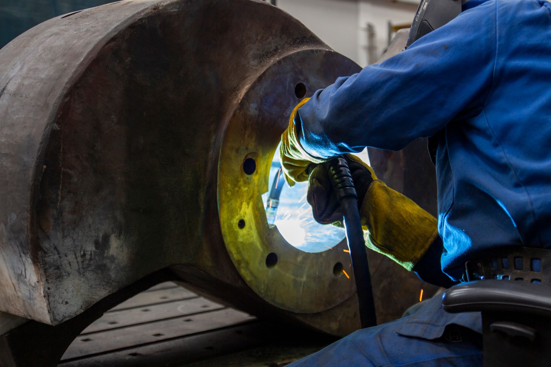 A metalworker welds a seam in a stainless-steel fabrication shop.