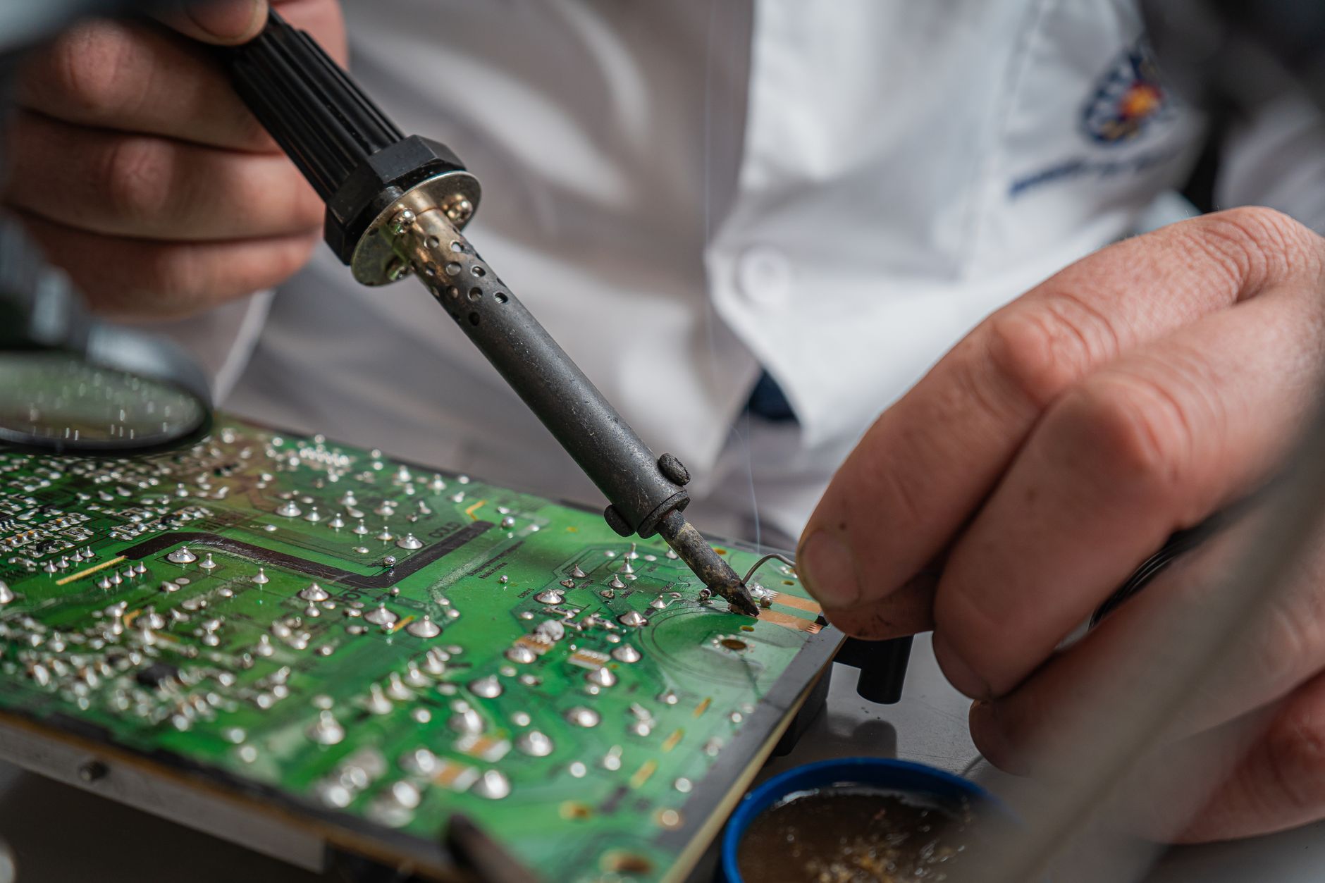 A technician solders small electronic components at a production workbench.