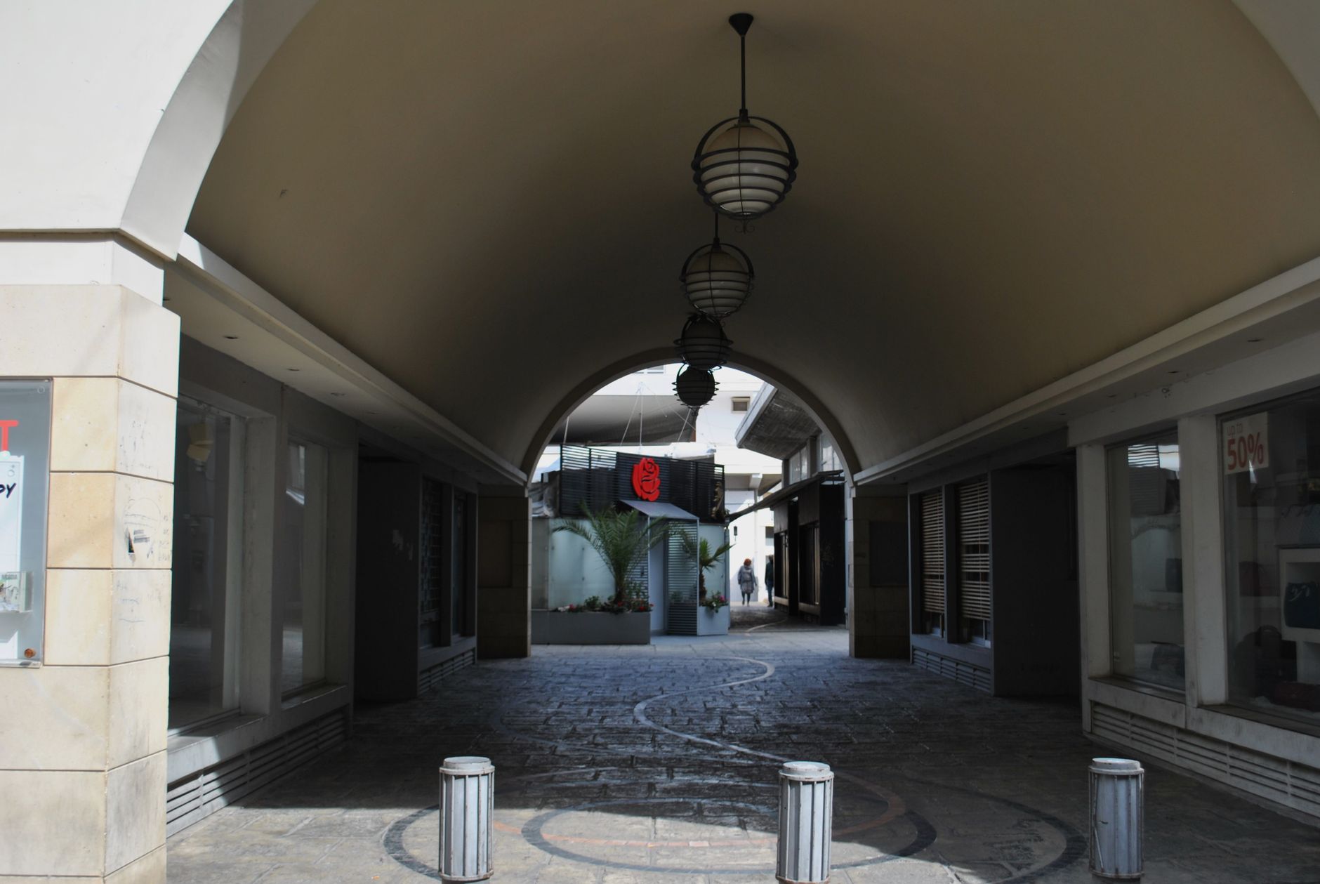 An open-air outlet center promenade with storefronts, pedestrian paths, and shoppers in daylight.