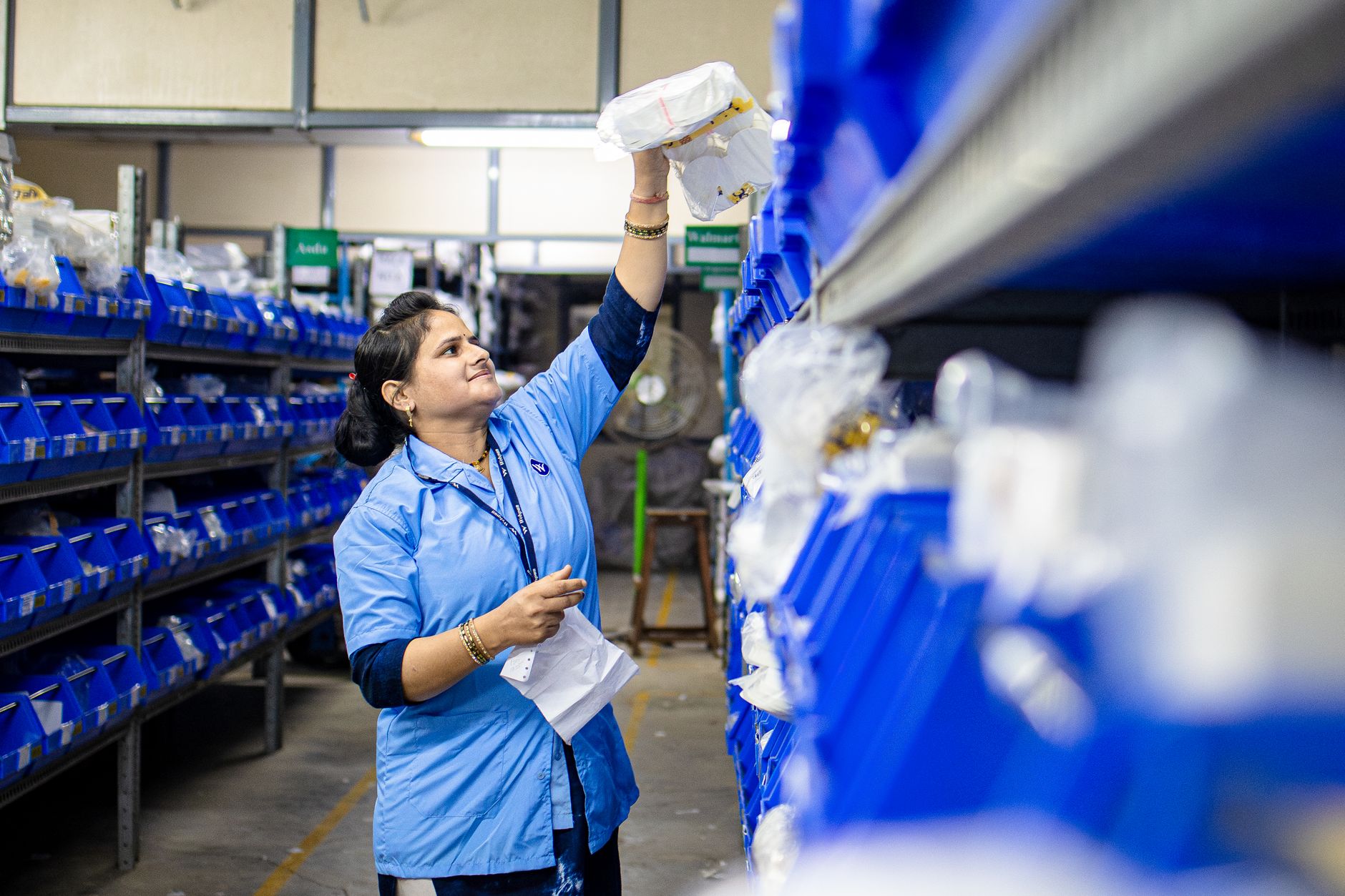 Warehouse associates pick outdoor apparel from tall shelving in a busy distribution center.