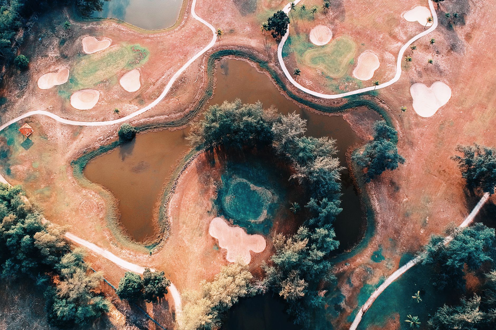 Drone shot of a scenic golf course with pathways and ponds, set in a vibrant landscape
