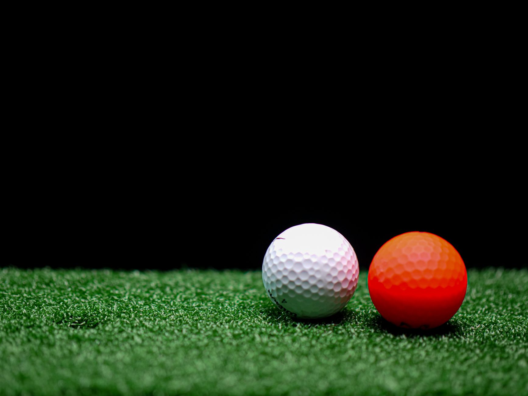 Close-up view of white and orange golf balls on artificial grass with a dark background