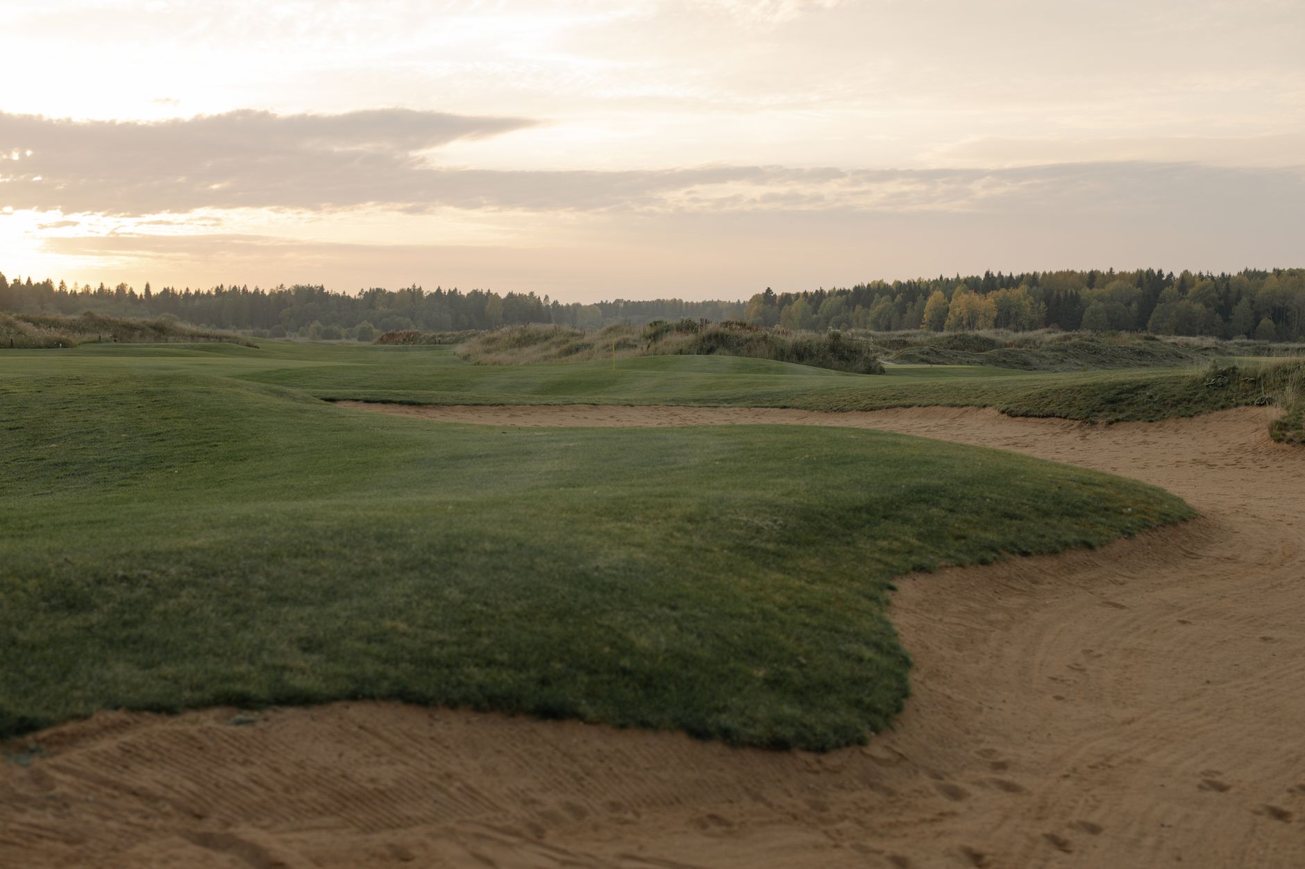 A tranquil golf course landscape at sunset, showcasing green fairways and gentle sandtraps