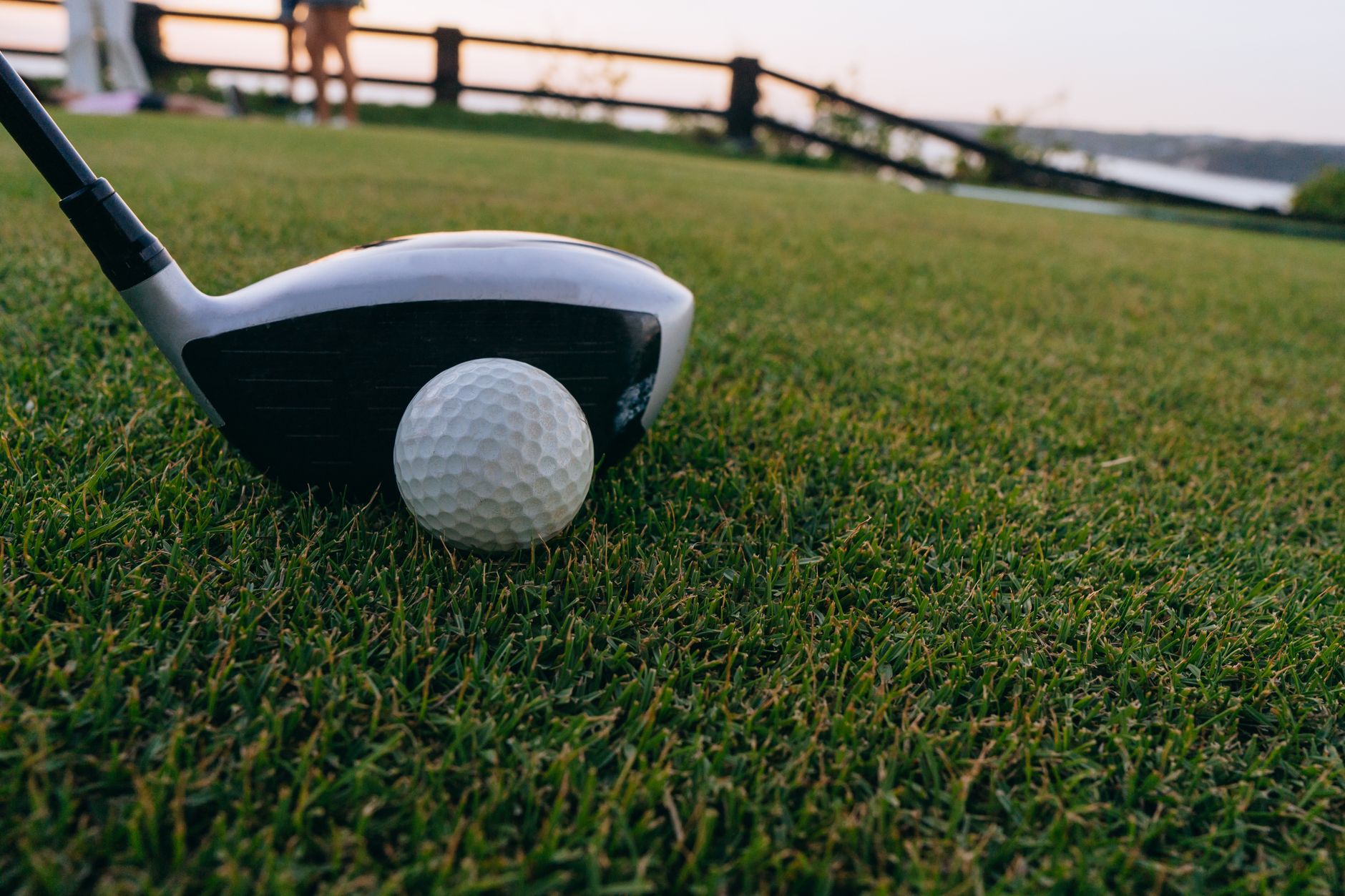 A close-up image of a golf ball and club on lush grass during sunset