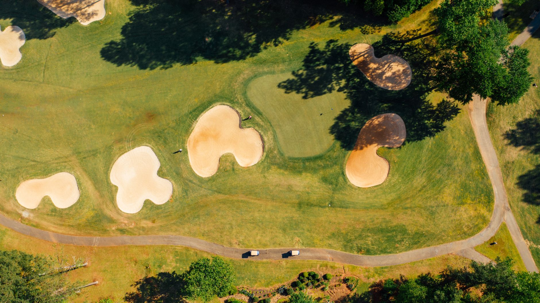 Aerial view of grass golf course with sandy bunkers near trees and narrow roadway in countryside