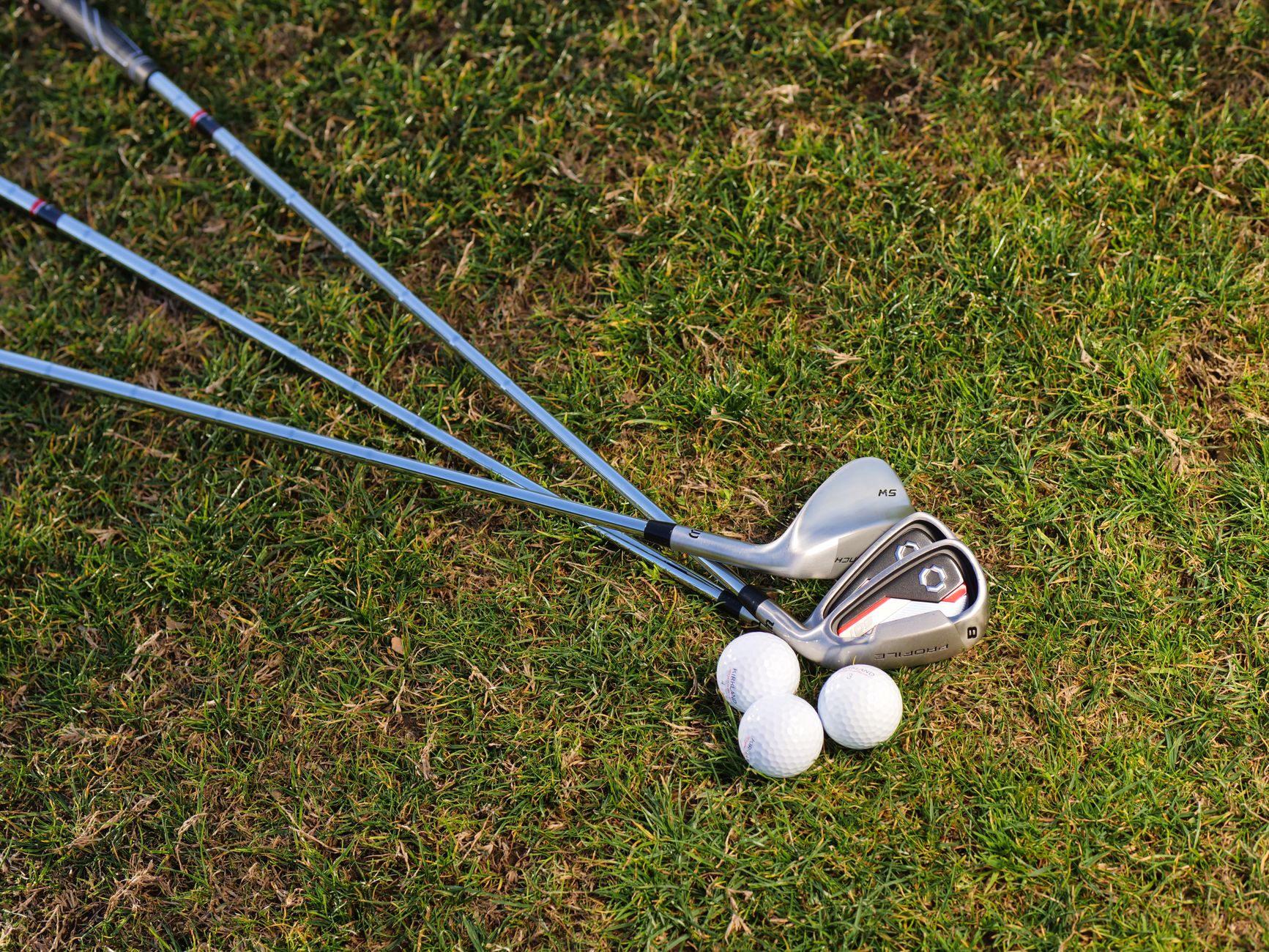 A set of golf irons with golf balls on a sunny grass field, perfect for golfing enthusiasts