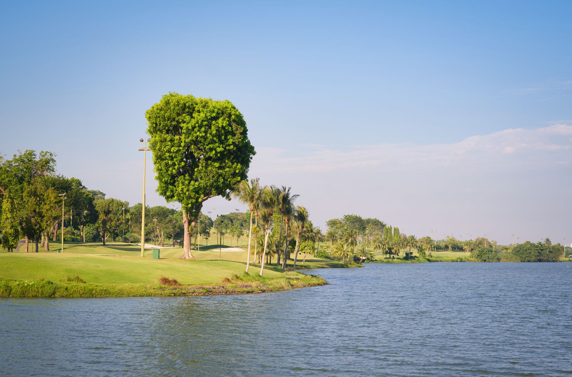 Beautiful view of a green golf course and lake under a bright blue sky, evoking tranquility and leisure