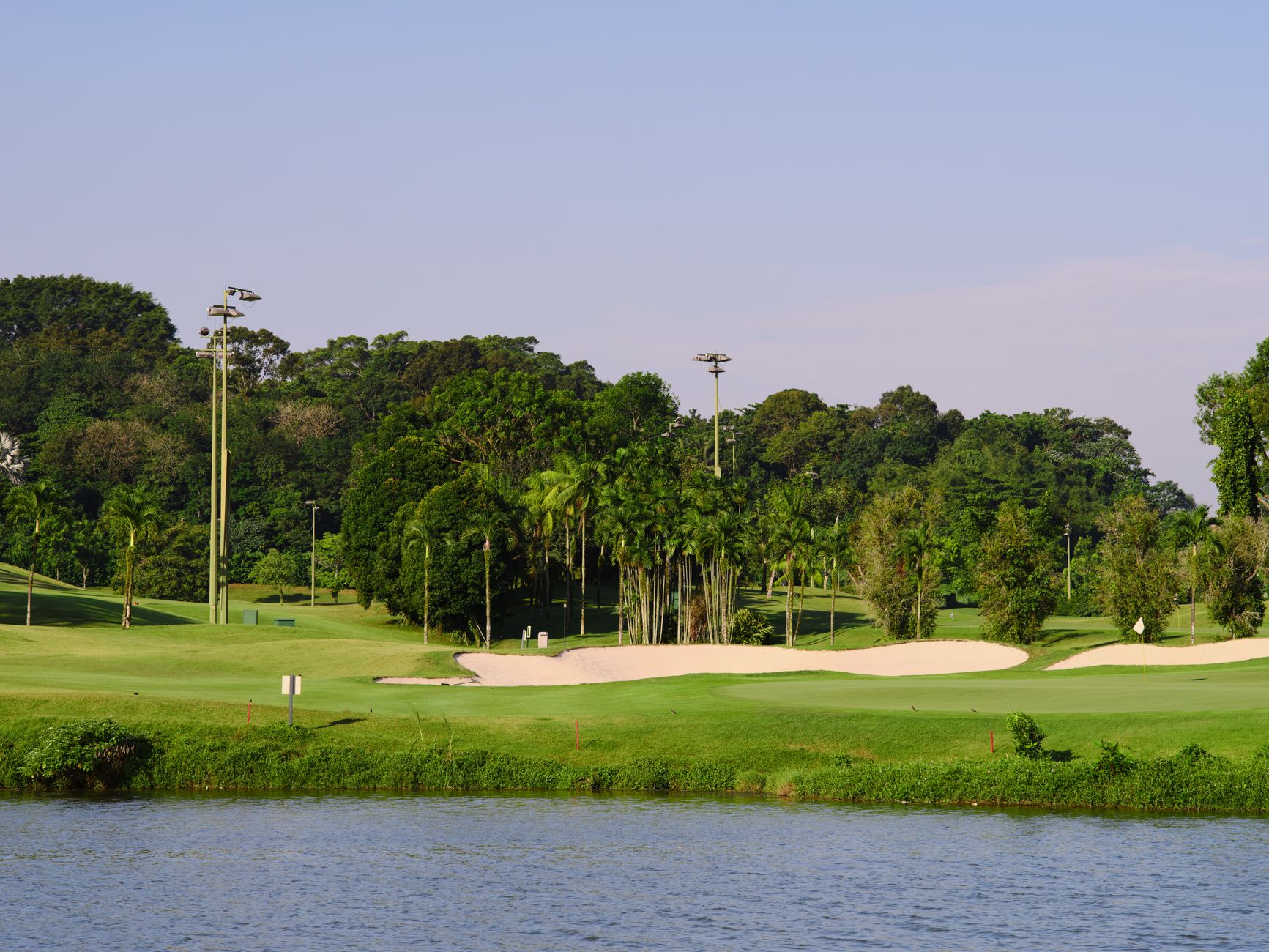 Peaceful golf course with lush greenery and sand traps by a river under a clear blue sky