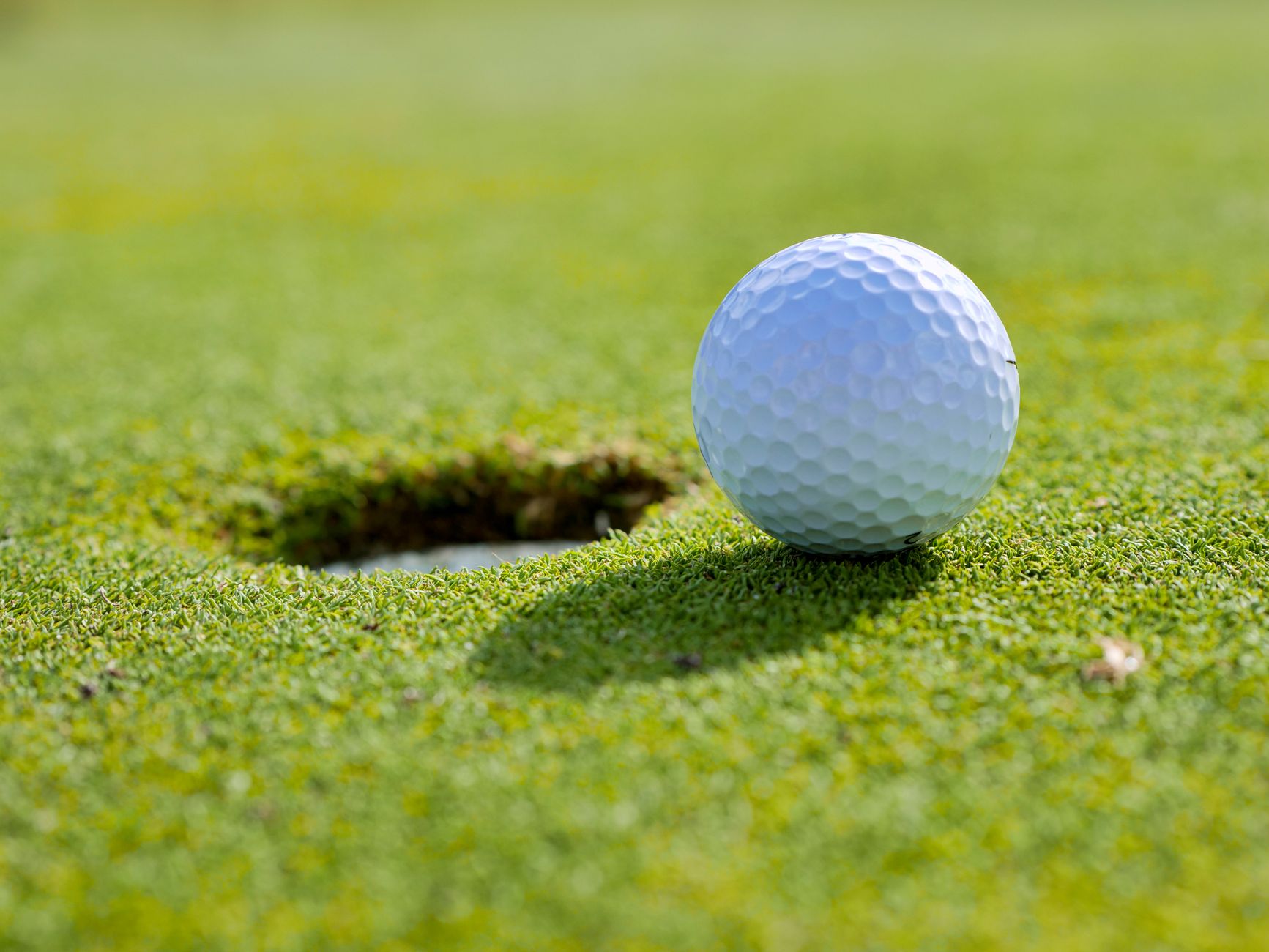 Close-up of a golf ball near the hole on a sunlit golf course green