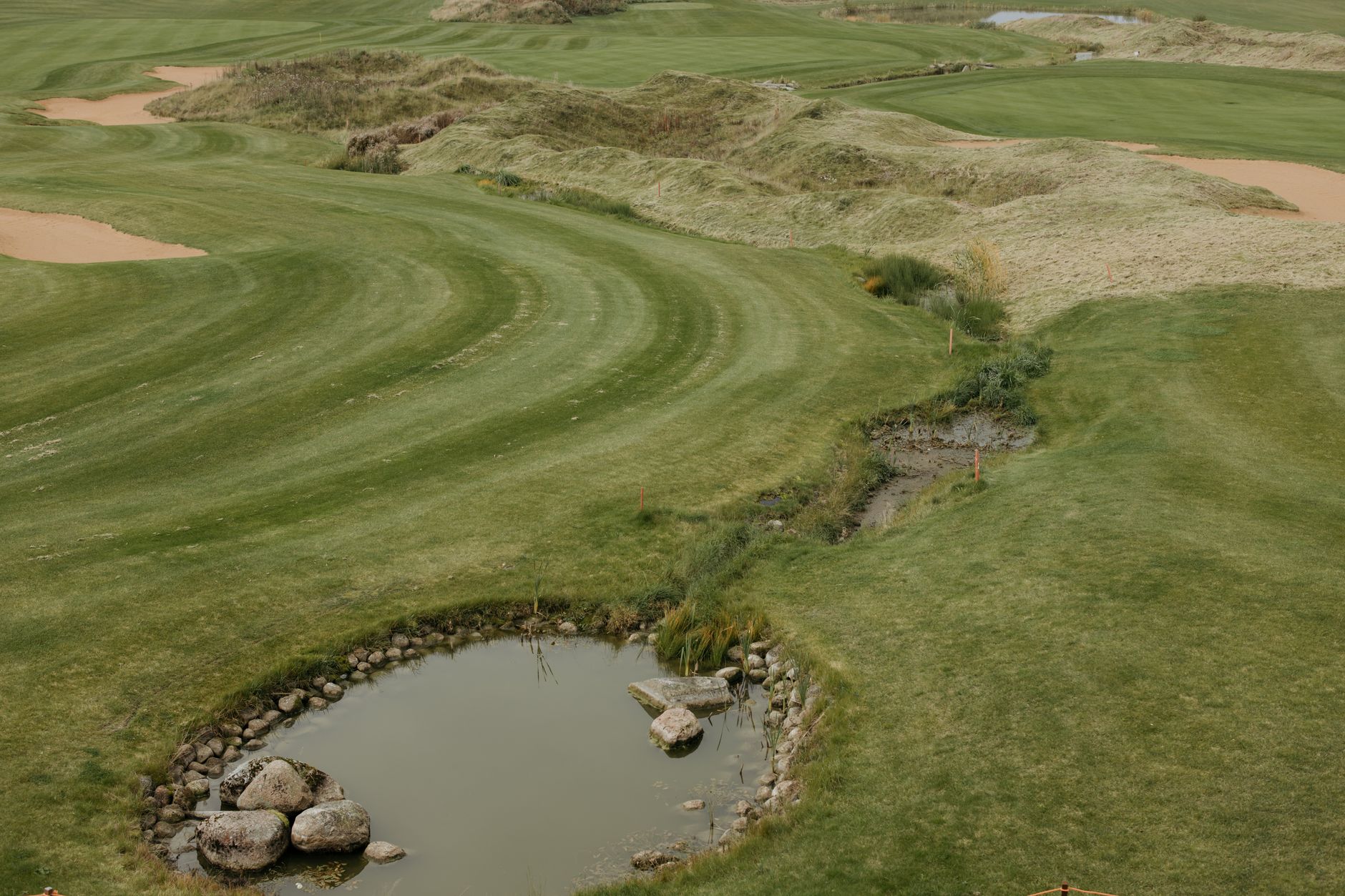 Beautiful drone shot of a lush green golf course with pond and rolling hills