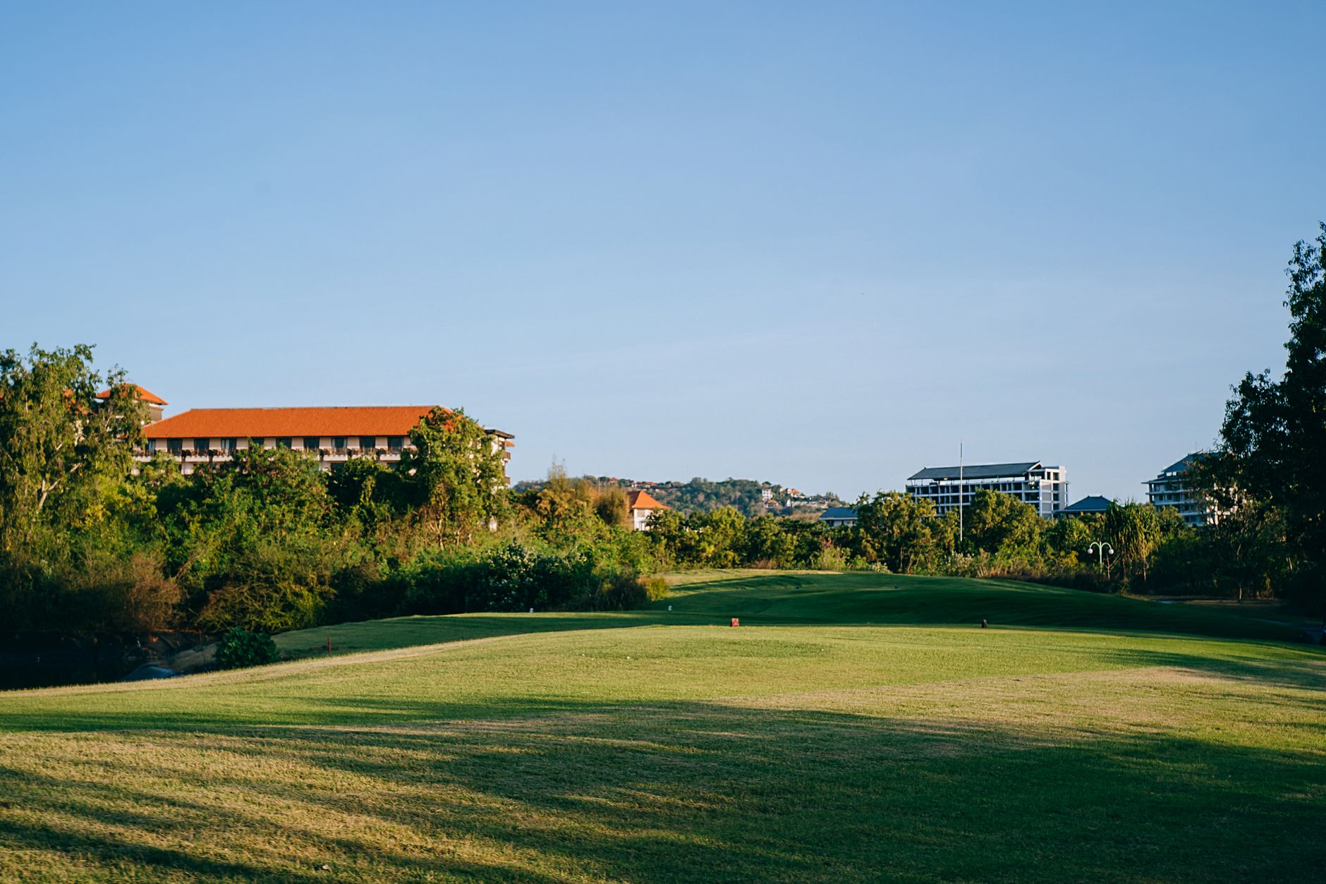 Scenic view of a golf course surrounded by greenery and residential buildings under a clear blue sky