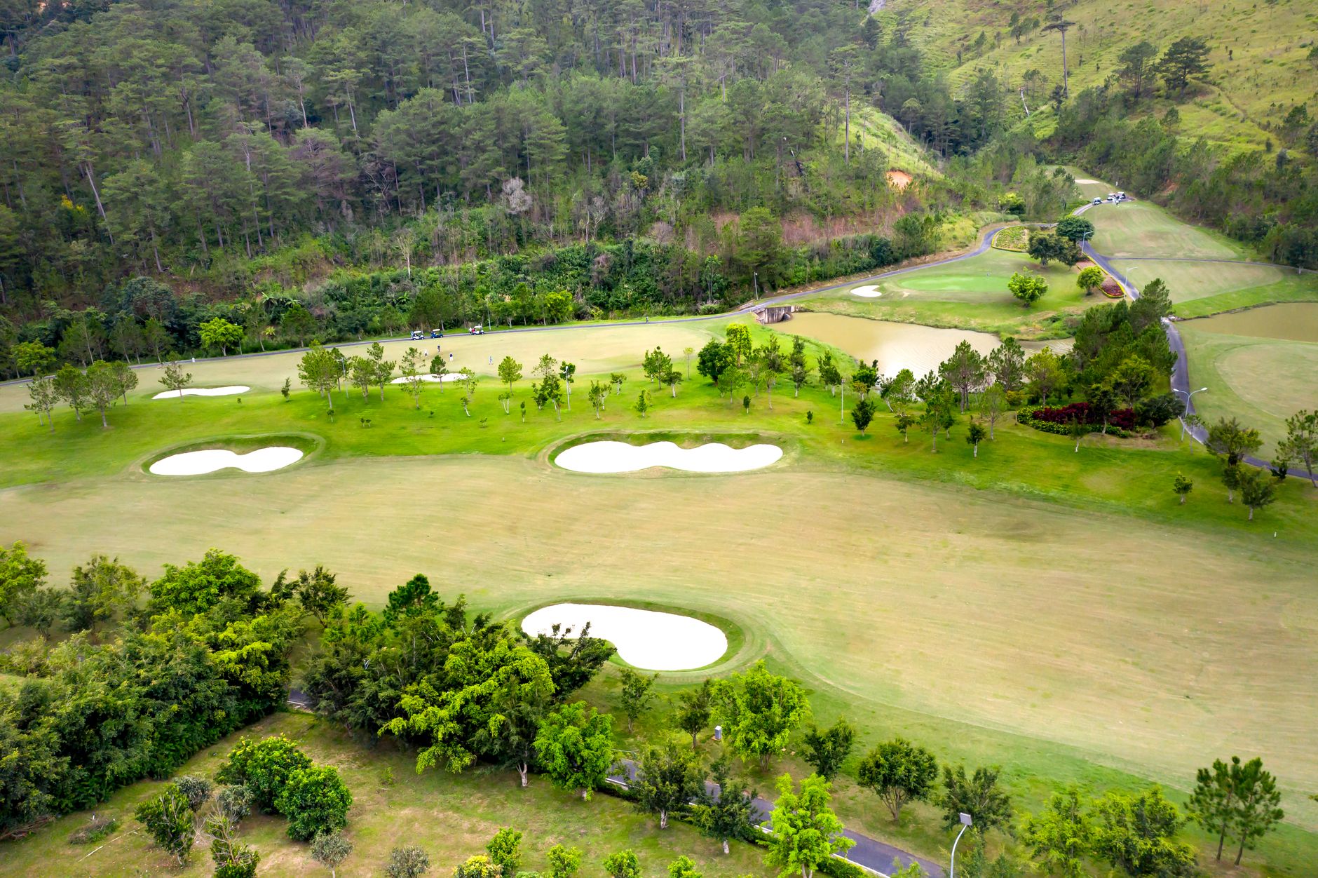 Aerial shot of a lush green golf course surrounded by nature and hills
