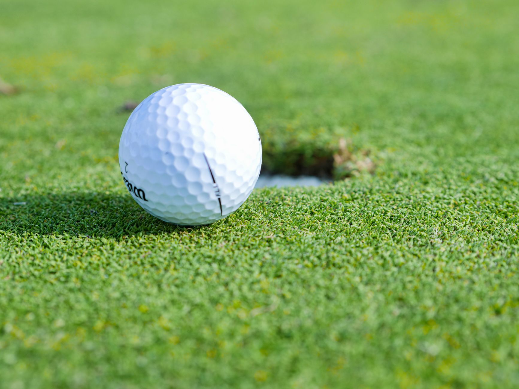 A close-up image of a golf ball near a hole on a vibrant green golf course