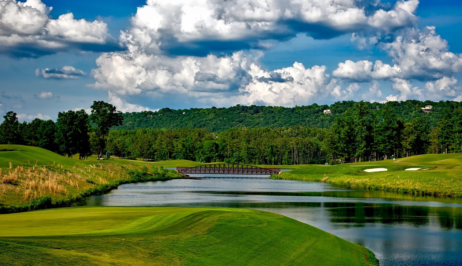 Scenic golf course with lush greenery, river, and a bridge under a bright summer sky