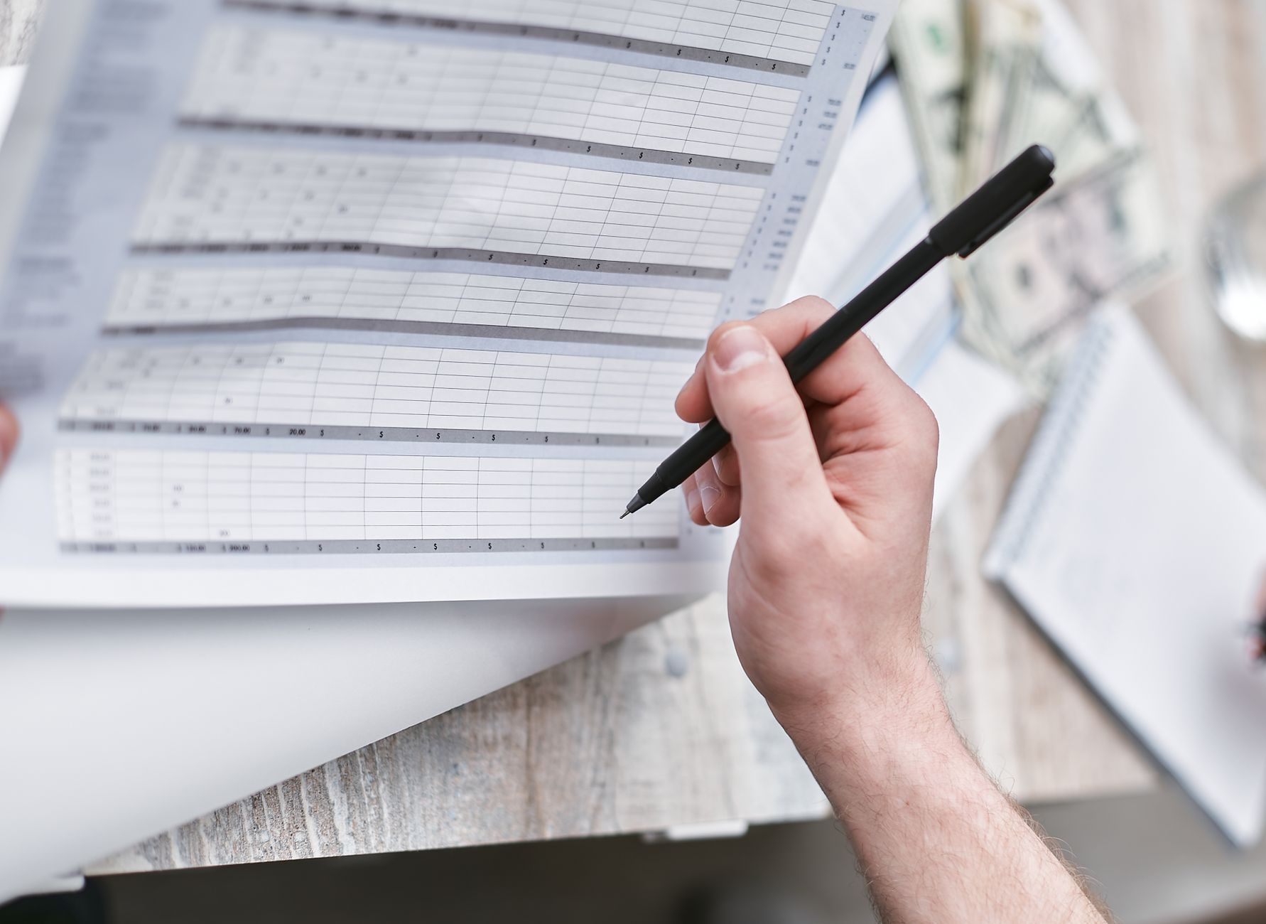 A desk covered with printed ledgers and a laptop showing budget figures.