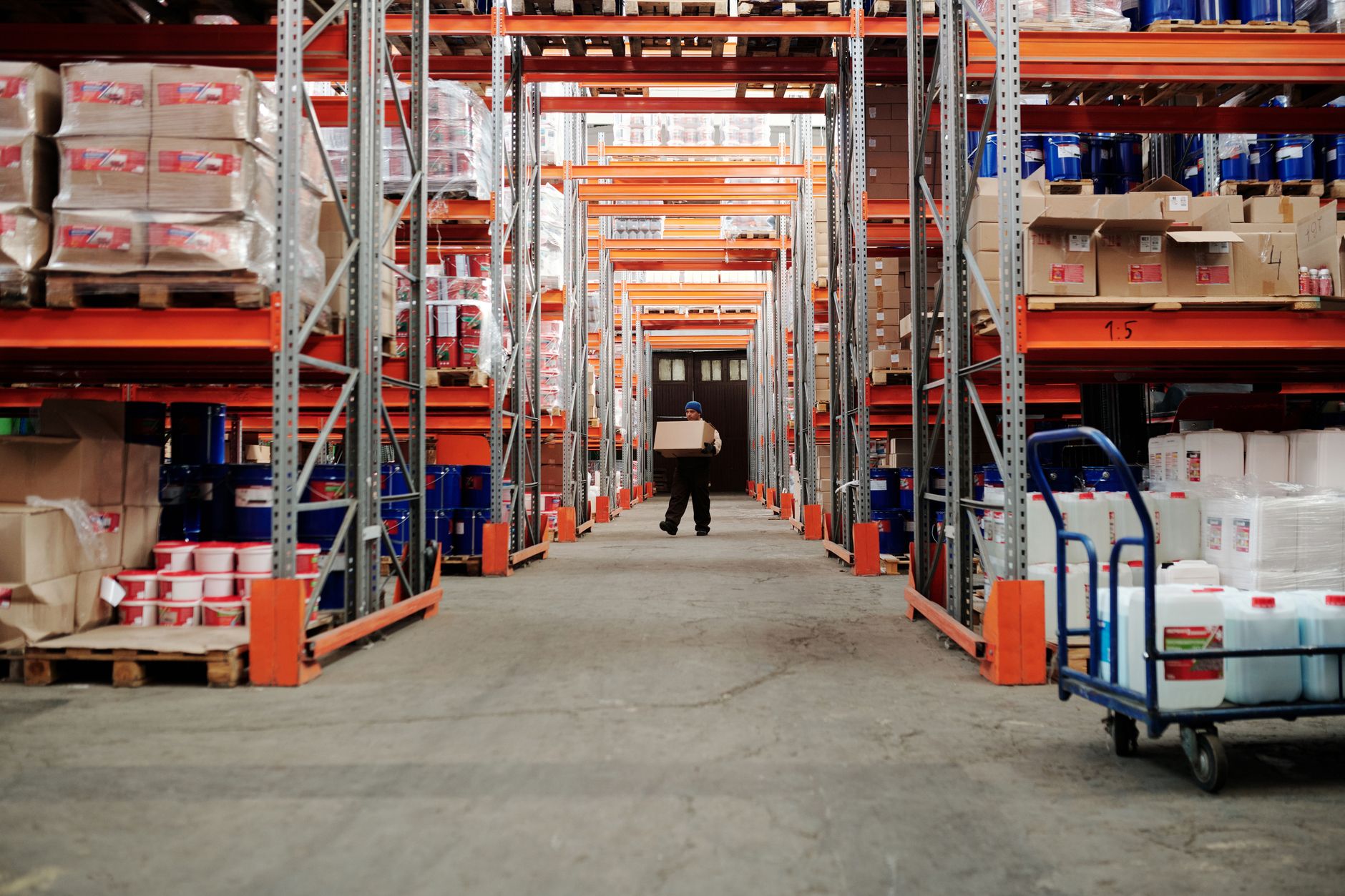 A narrow picking aisle between high racks of labelled parts bins in a distribution warehouse.