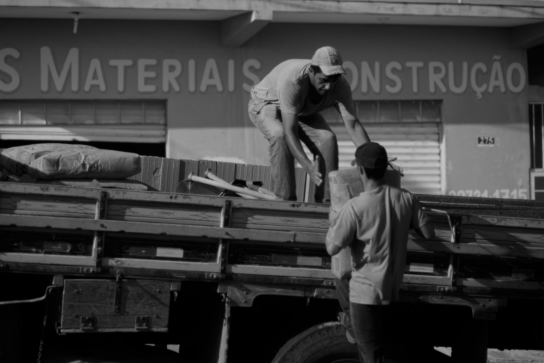 Two workers in work clothes loading building materials at the edge of a supply yard.