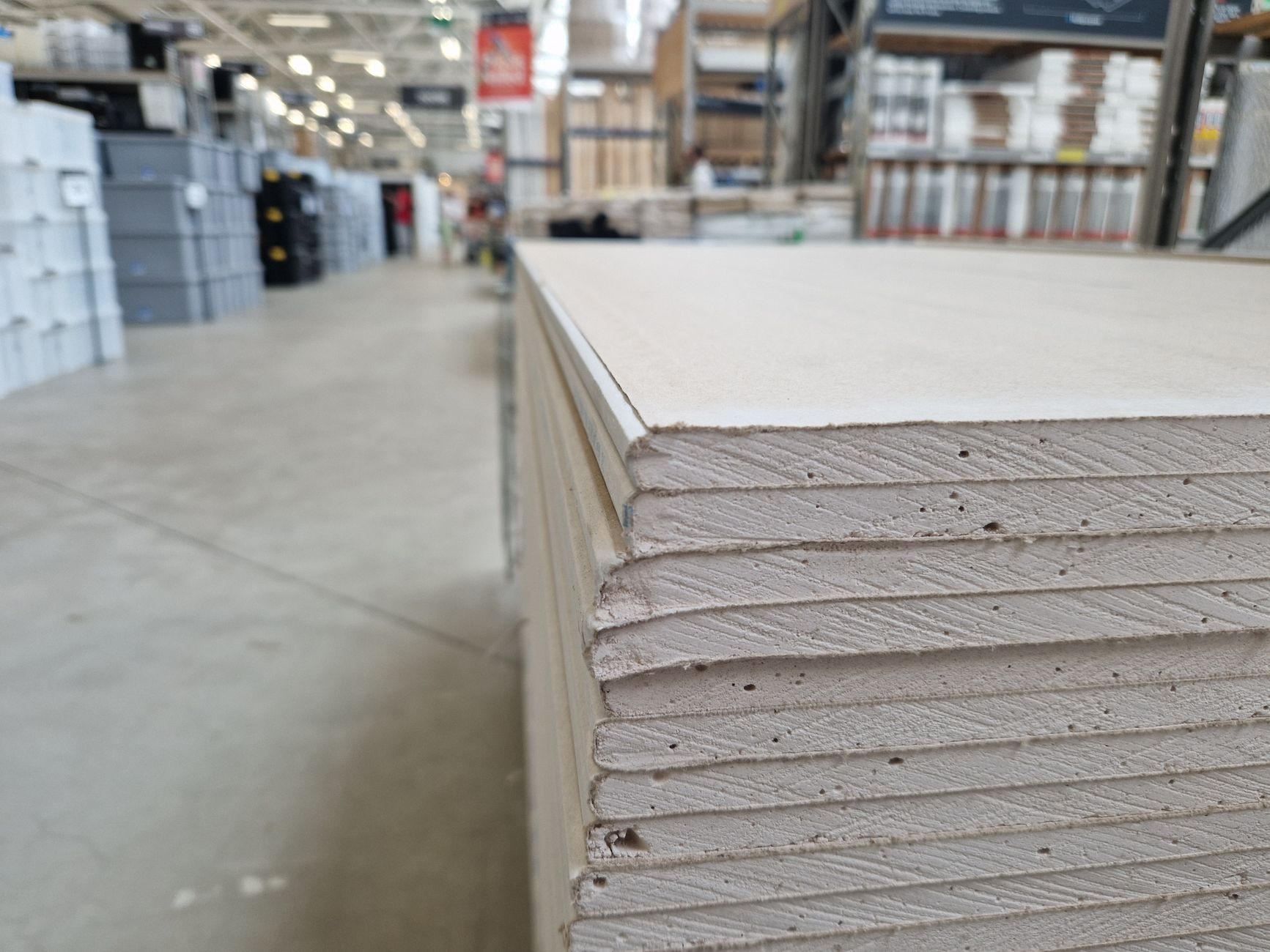 Stacks of drywall sheets and lumber neatly organised on pallets in a building materials warehouse.