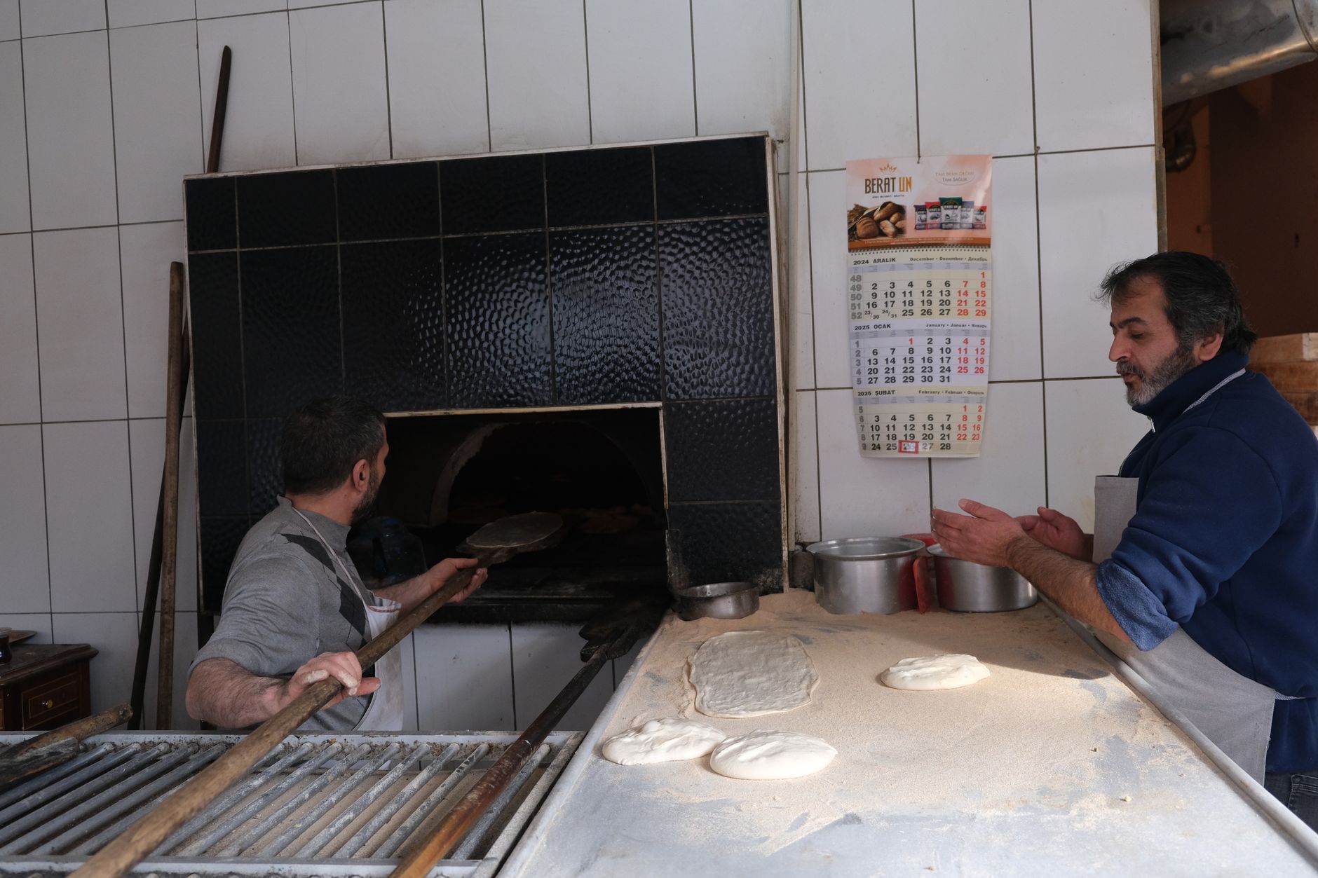 Two bakers in aprons working side by side at a floured kitchen counter.