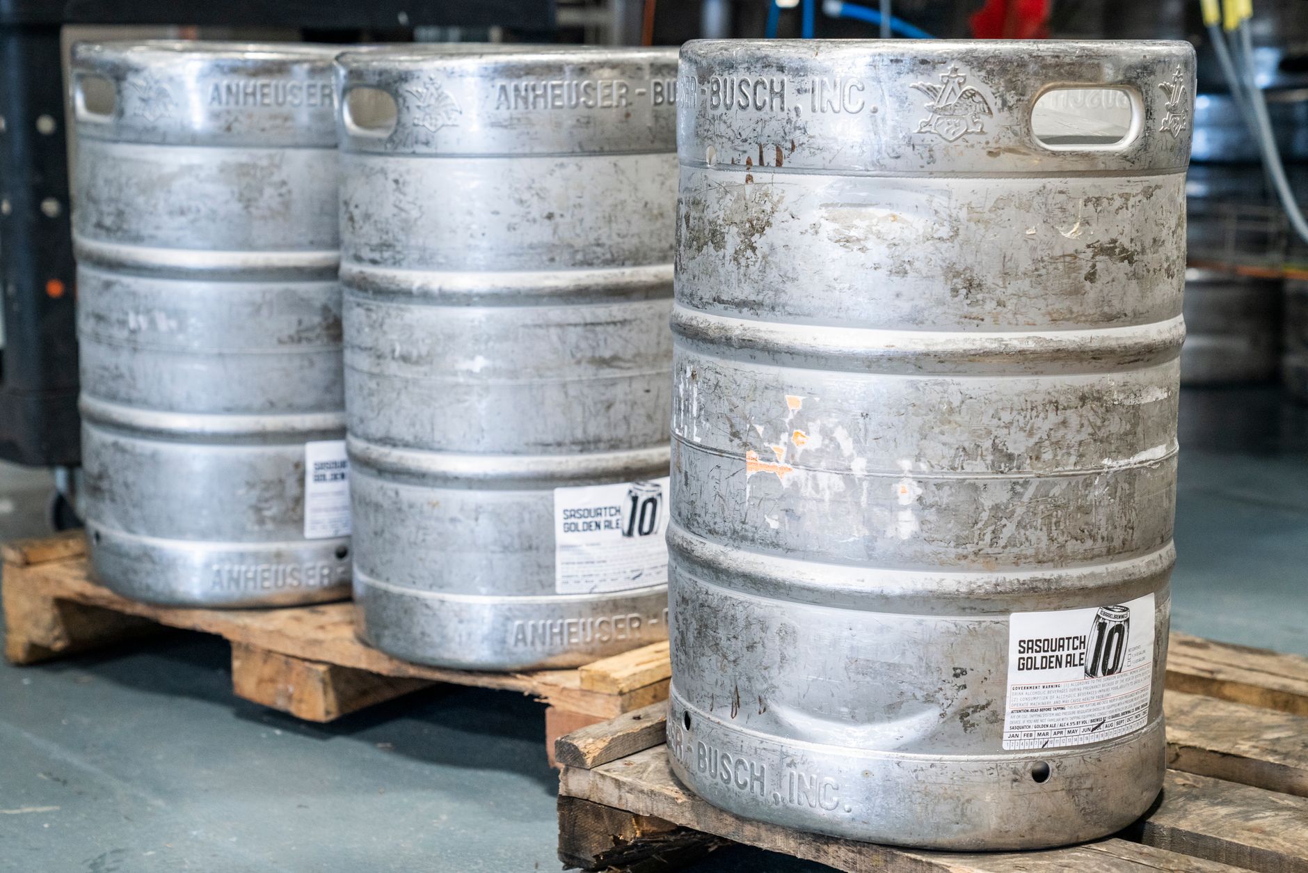 Rows of stacked kegs sit on pallets in a storage area beside the brewing space.