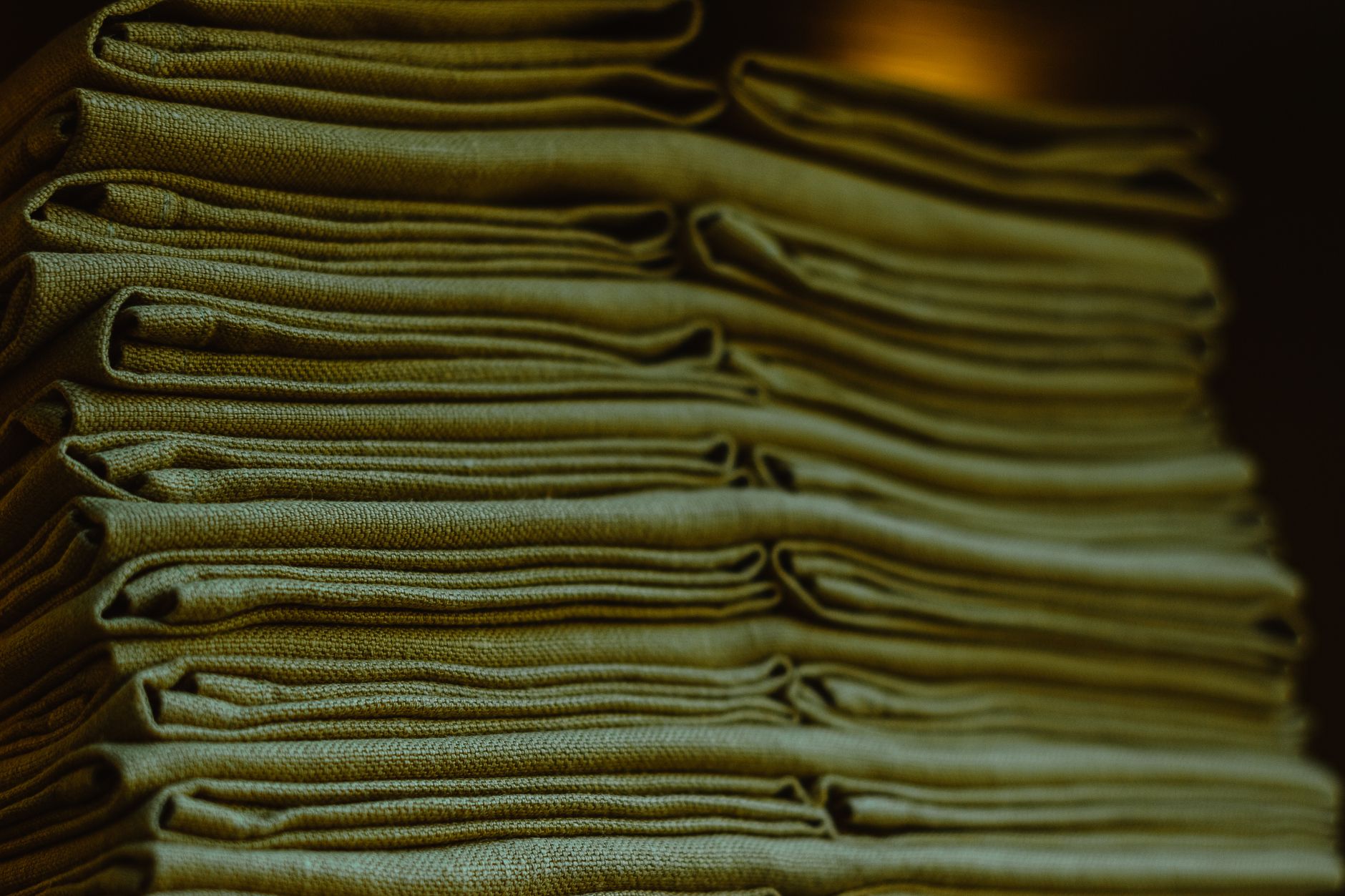 Stacks of folded white linen sheets and towels sit ready for distribution in a laundry department.