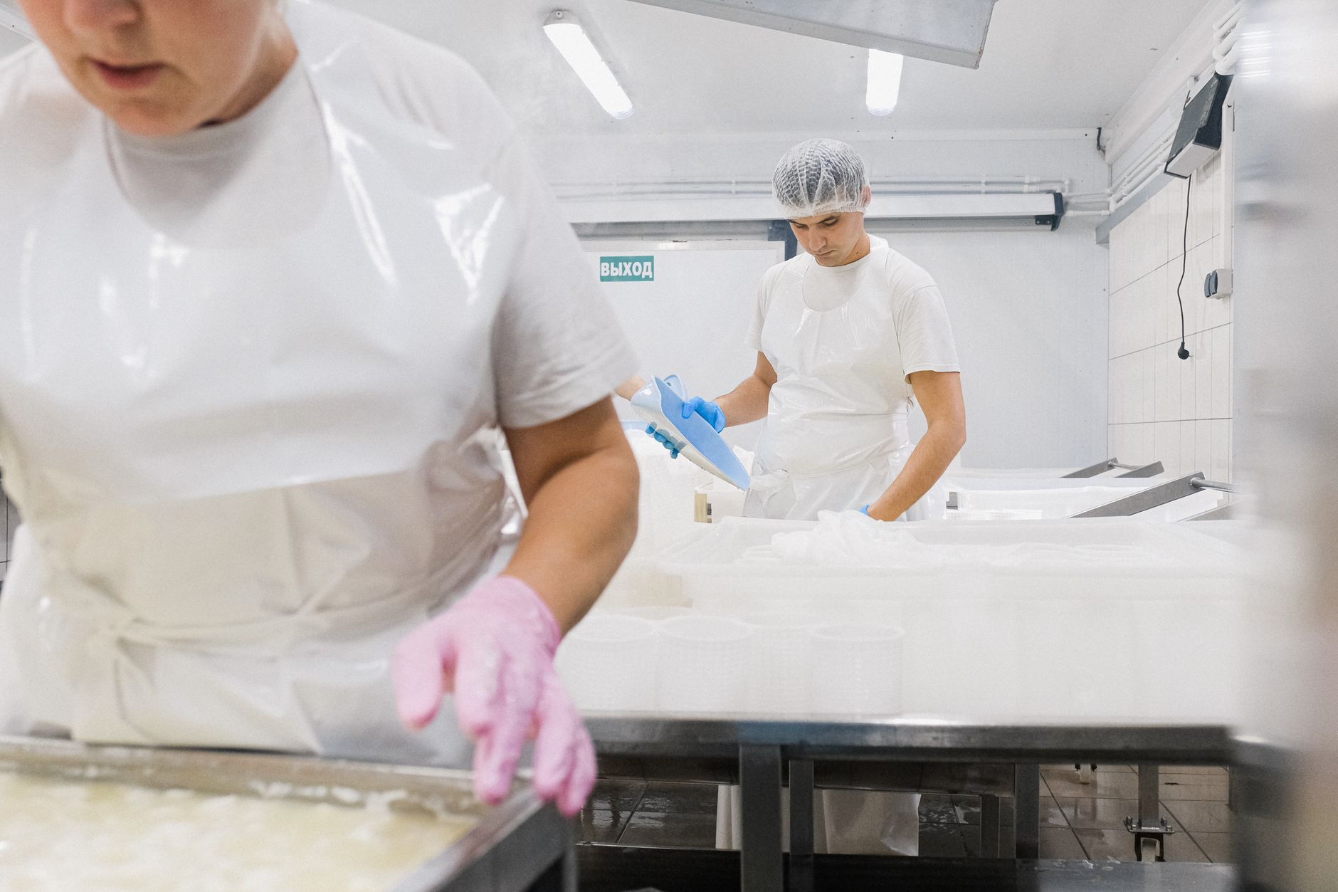 Two food plant employees in hairnets and protective gear talk beside a processing station.
