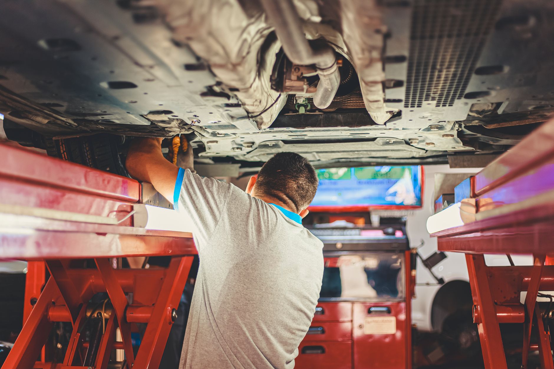 A mechanic works on a vehicle in a workshop with tools and parts scattered around the floor.