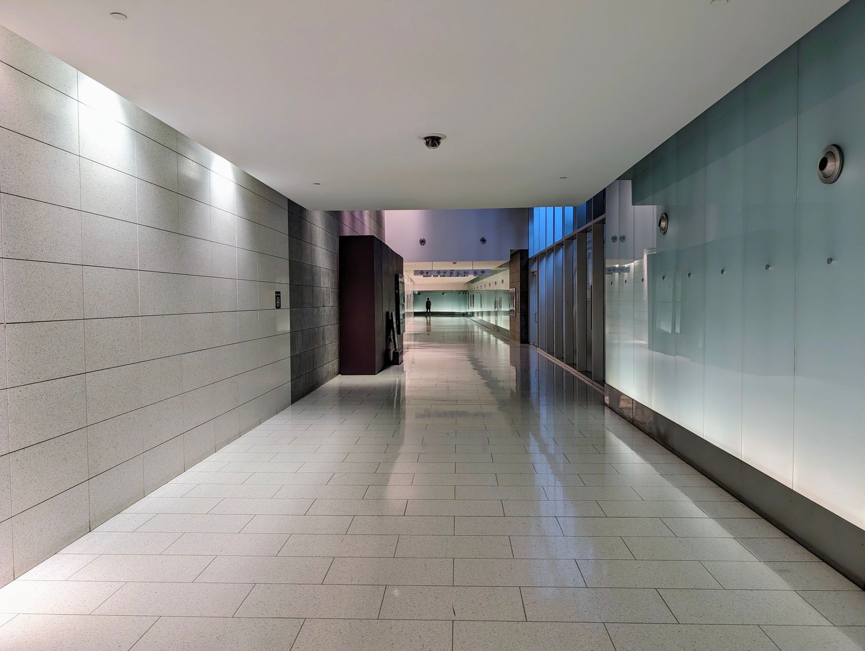 Wide corridor with hard flooring leading toward a bright lobby entrance.