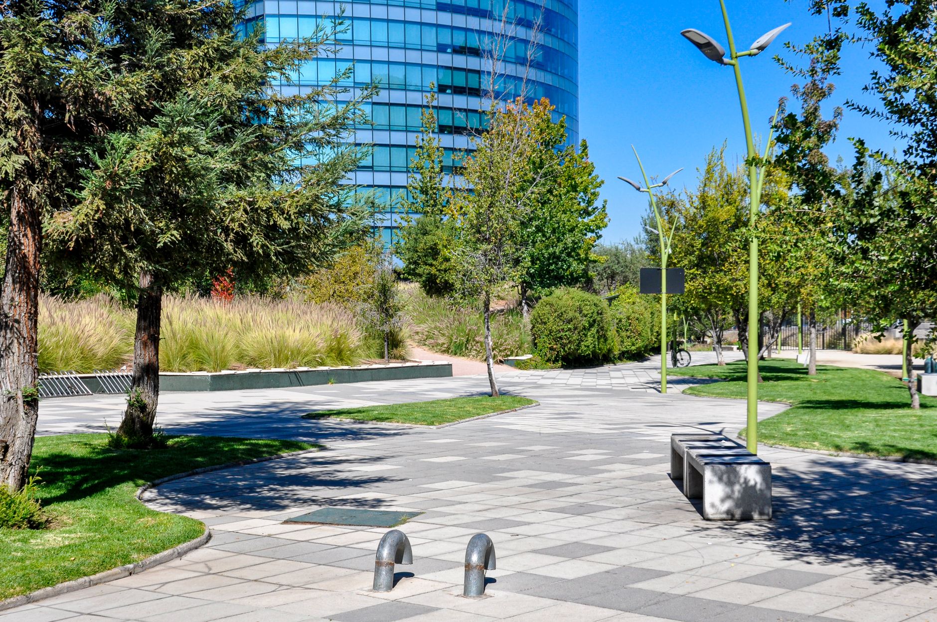 A paved walkway winding past lawn and landscaped beds outside low office buildings on a business campus.